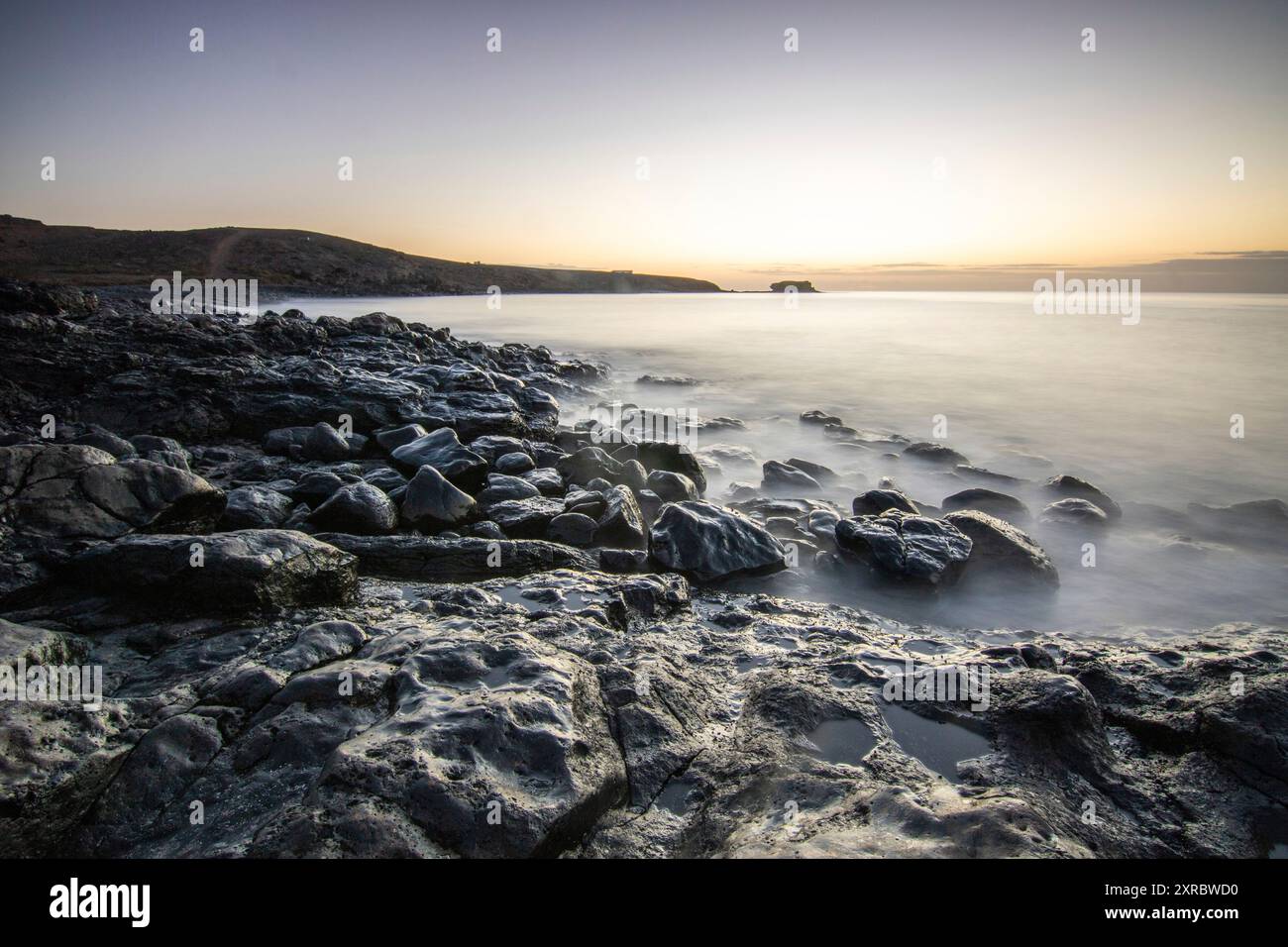 Blick auf den Sonnenaufgang über dem Atlantik. Blick über einen Steinstrand auf einer Vulkaninsel. Kalte Lavasteine am Meer am Strand von Playa Laja del Corral, Fuerteventura, Kanarischen Inseln, Spanien Stockfoto