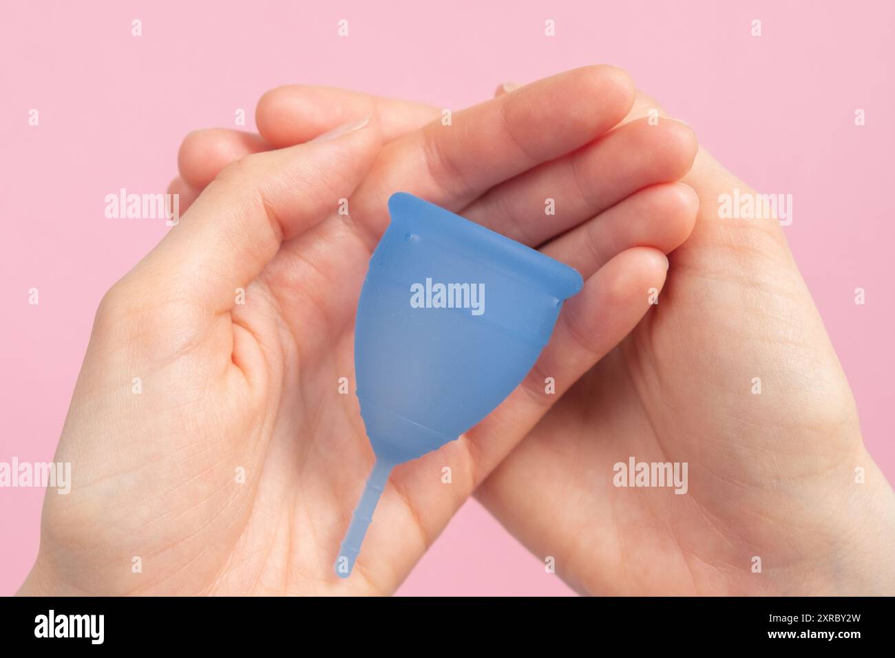 Frauenhände halten blaue Menstruationstasse vor rosa Hintergrund, Damenhygiene, nachhaltige Periodenpflege. Keine Verschwendung, schonend für die Umwelt. Stockfoto