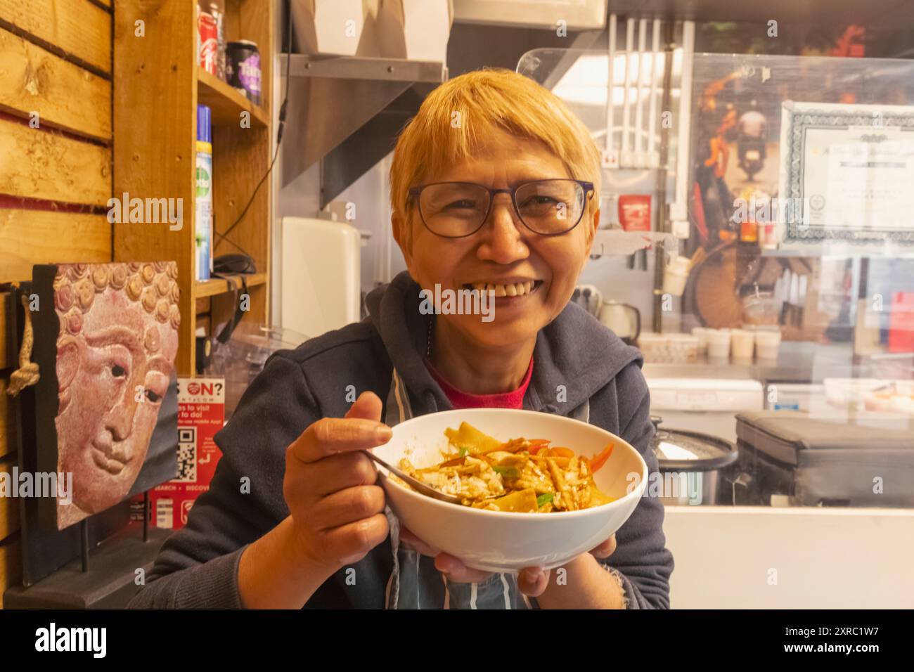 England, Kent, Folkestone, Folkestone Harbour, Smiling Thai Take-Away Food Owner essen eine Schüssel thailändischer Speisen Stockfoto