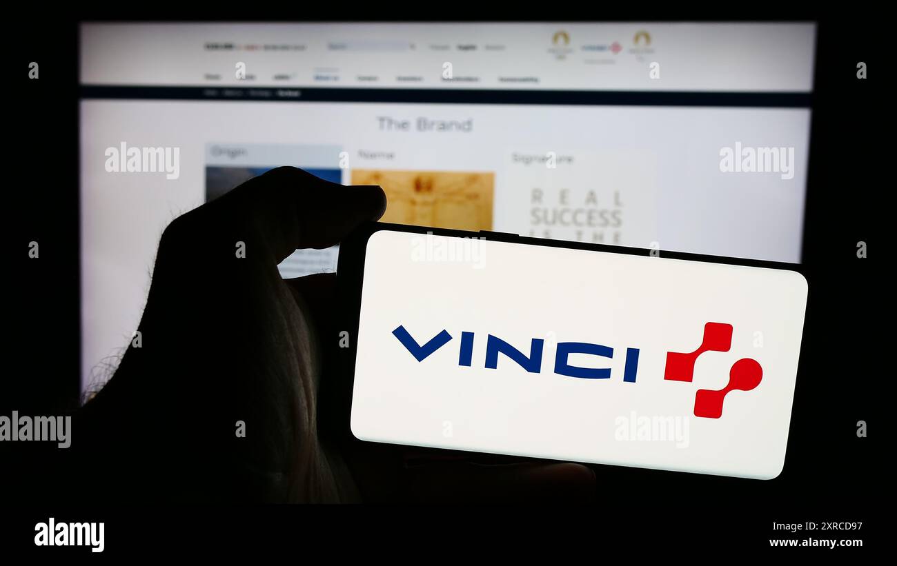 Person mit Smartphone und Logo des französischen Konzessionsunternehmens Vinci S.A. vor der Website. Schwerpunkt auf dem Display des Telefons. Stockfoto