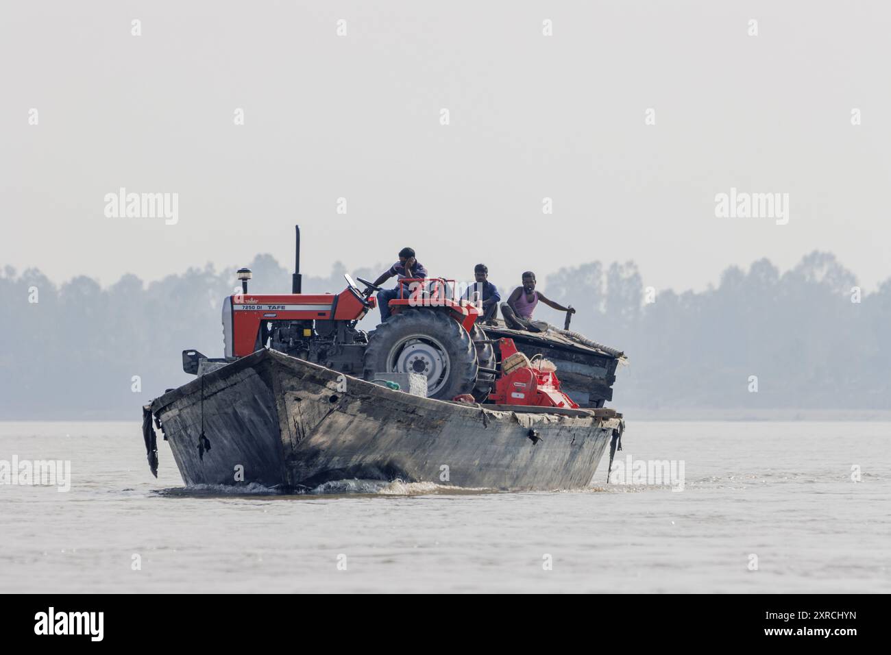 Ein neuer Traktor wird auf einem traditionellen Boot ausgeliefert. Der von den Überschwemmungen zurückgelassene Schlamm macht die Chars sehr fruchtbar und für den Anbau vieler Sorten von Kulturen geeignet. Das Risiko ist hoch; alles investierte kann innerhalb von Sekunden von einer Überschwemmung weggespült werden. Stockfoto