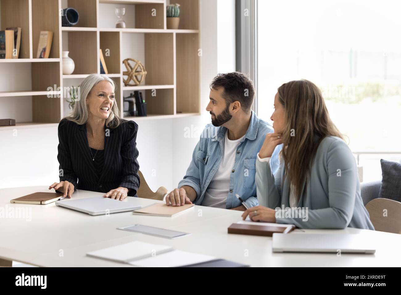 Glückliche ältere Unternehmensberaterin, die mit jüngeren Kollegen spricht Stockfoto