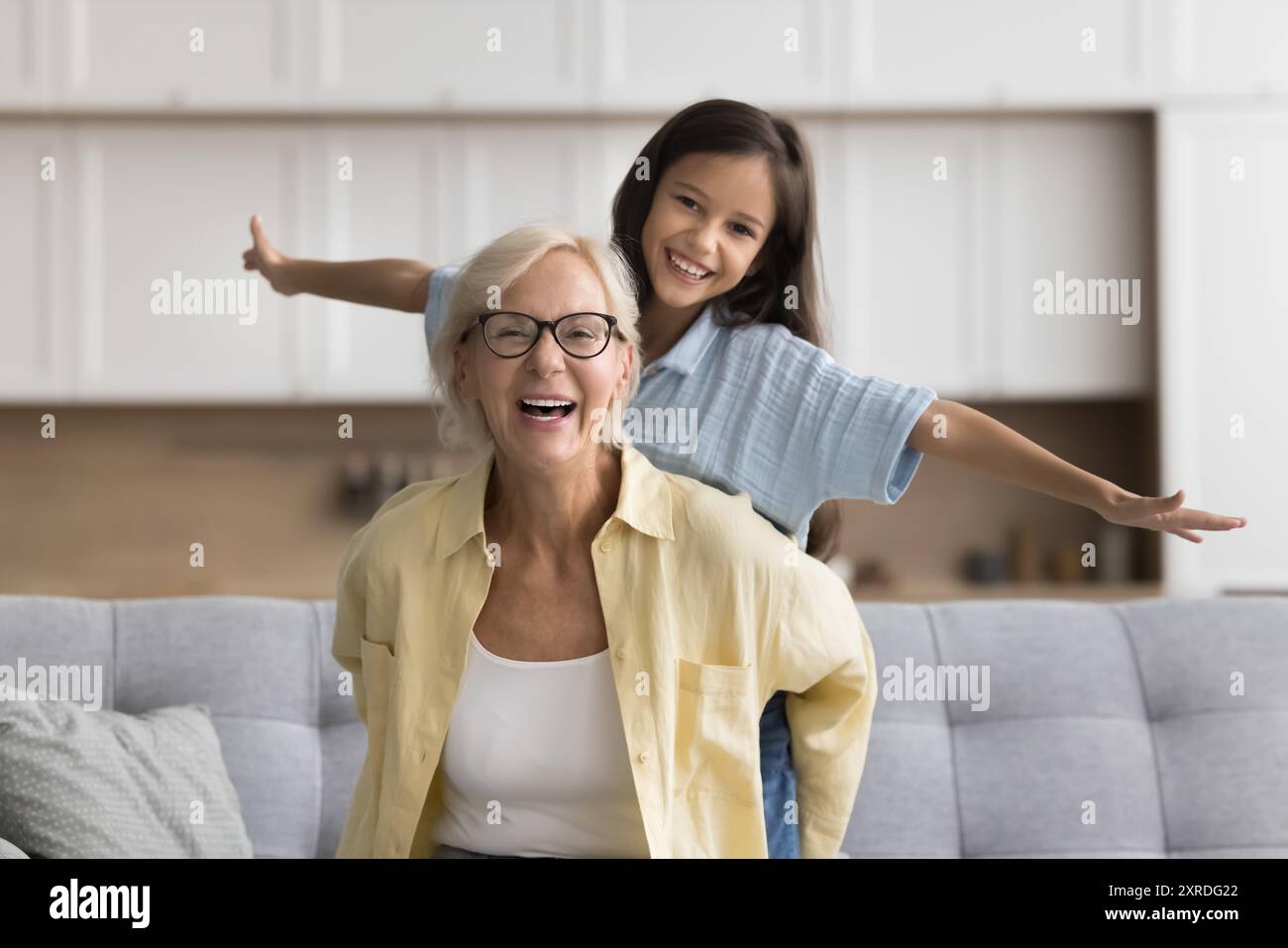 Aktive blonde Oma, die ein süßes, hübsches Mädchen von hinten hält Stockfoto