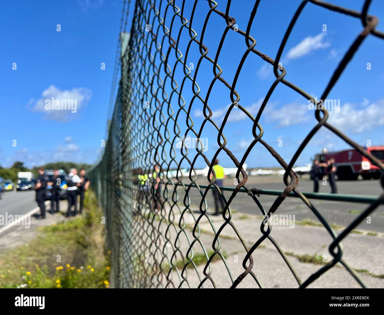 Schleswig-Holstein. August 2024. Polizei und Feuerwehr stehen am Flughafen auf der nordfriesischen Insel Sylt, wo Aktivisten der letzten Generation versuchten, einen Farbangriff auf einen Privatjet durchzuführen. Zwei Demonstranten der Klimainitiative der letzten Generation haben sich am Samstag neben einem Privatjet am Flughafen Sylt am Boden festgehalten. Der Versuch, den Privatjet zu lackieren, scheiterte an der raschen Intervention des Flughafenpersonals, wie ein Reporter der Deutschen Presseagentur feststellte. Die Aktivisten hatten zuvor ein Loch in den Zaun des Flughafengeländes geschnitten, wo Credit:dpa/Alam Stockfoto