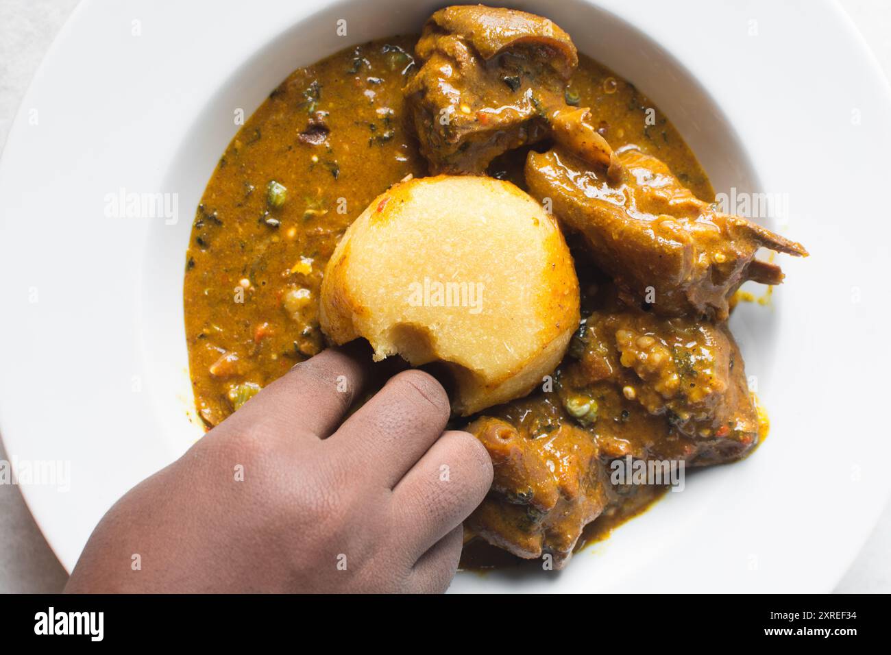 Blick von oben auf nigerianische Ogbono-Suppe und eba auf einem weißen Teller, Blick von oben auf Ogbono-Suppe mit garri und verschiedenen Fleischsorten auf einem Suppenteller Stockfoto