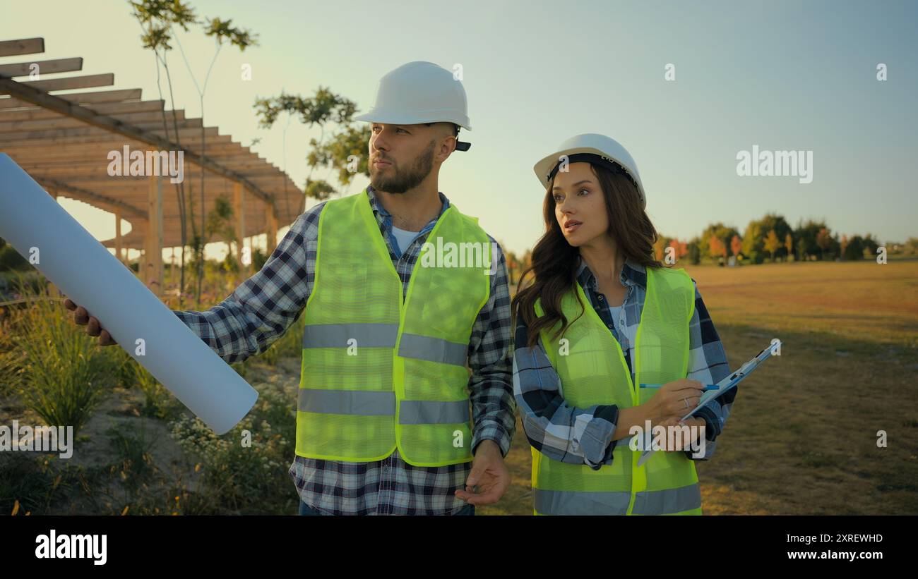 Kaukasische Kollegen Architektenpartnerschaft männlicher Mann Geschäftsmann Ingenieur halten Blueprint, der Talk erklärt weibliche Geschäftsfrau Inspektorin Frau schreibt Stockfoto