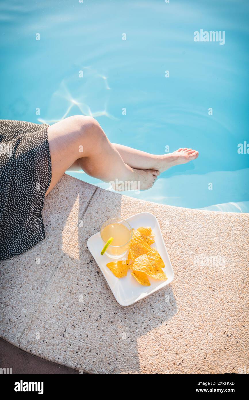 Genießen Sie an einem sonnigen Tag ein erfrischendes Glas Zitronenginger Kombucha mit Nachos am Pool Stockfoto