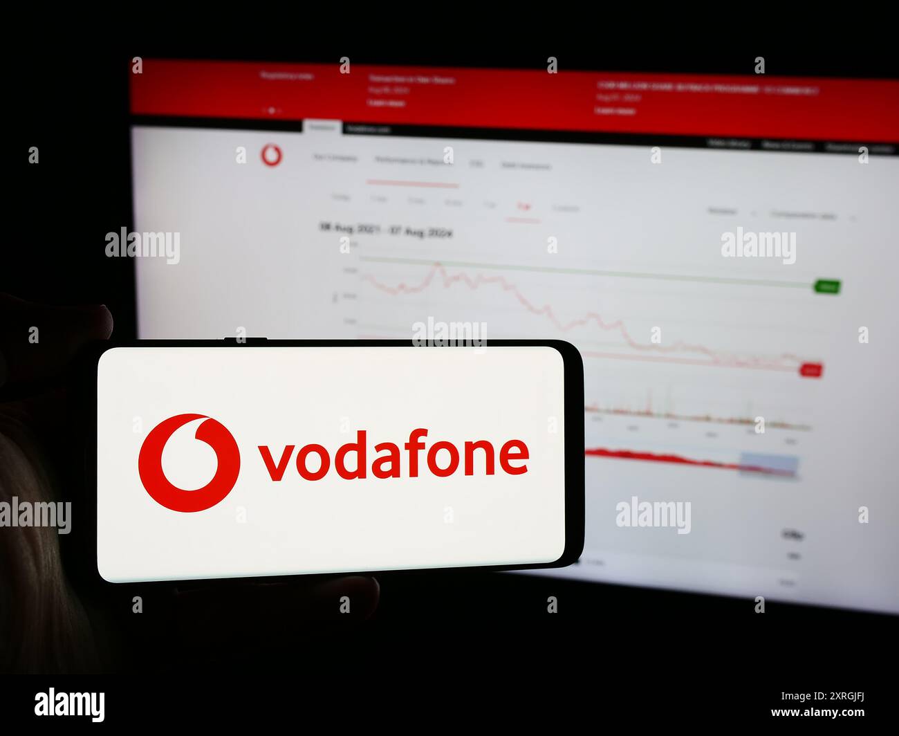 Person, die ein Mobiltelefon mit dem Logo des britischen Telekommunikationsunternehmens Vodafone Group plc vor der Webseite hält. Schwerpunkt auf dem Display des Telefons. Stockfoto