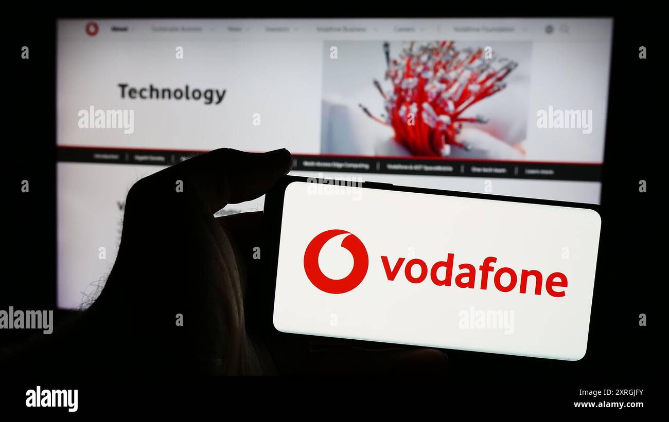 Person mit Smartphone und Logo des britischen Telekommunikationsunternehmens Vodafone Group plc vor der Website. Schwerpunkt auf dem Display des Telefons. Stockfoto