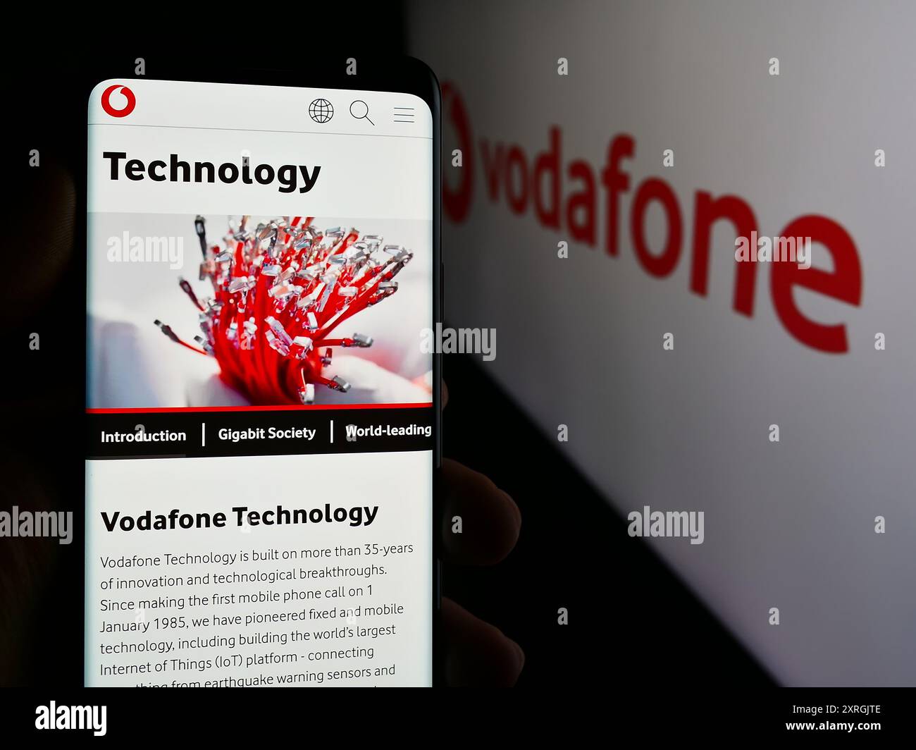 Person, die ein Mobiltelefon hält, mit Webseite des britischen Telekommunikationsunternehmens Vodafone Group plc vor dem Logo. Konzentrieren Sie sich auf die Mitte des Telefondisplays. Stockfoto