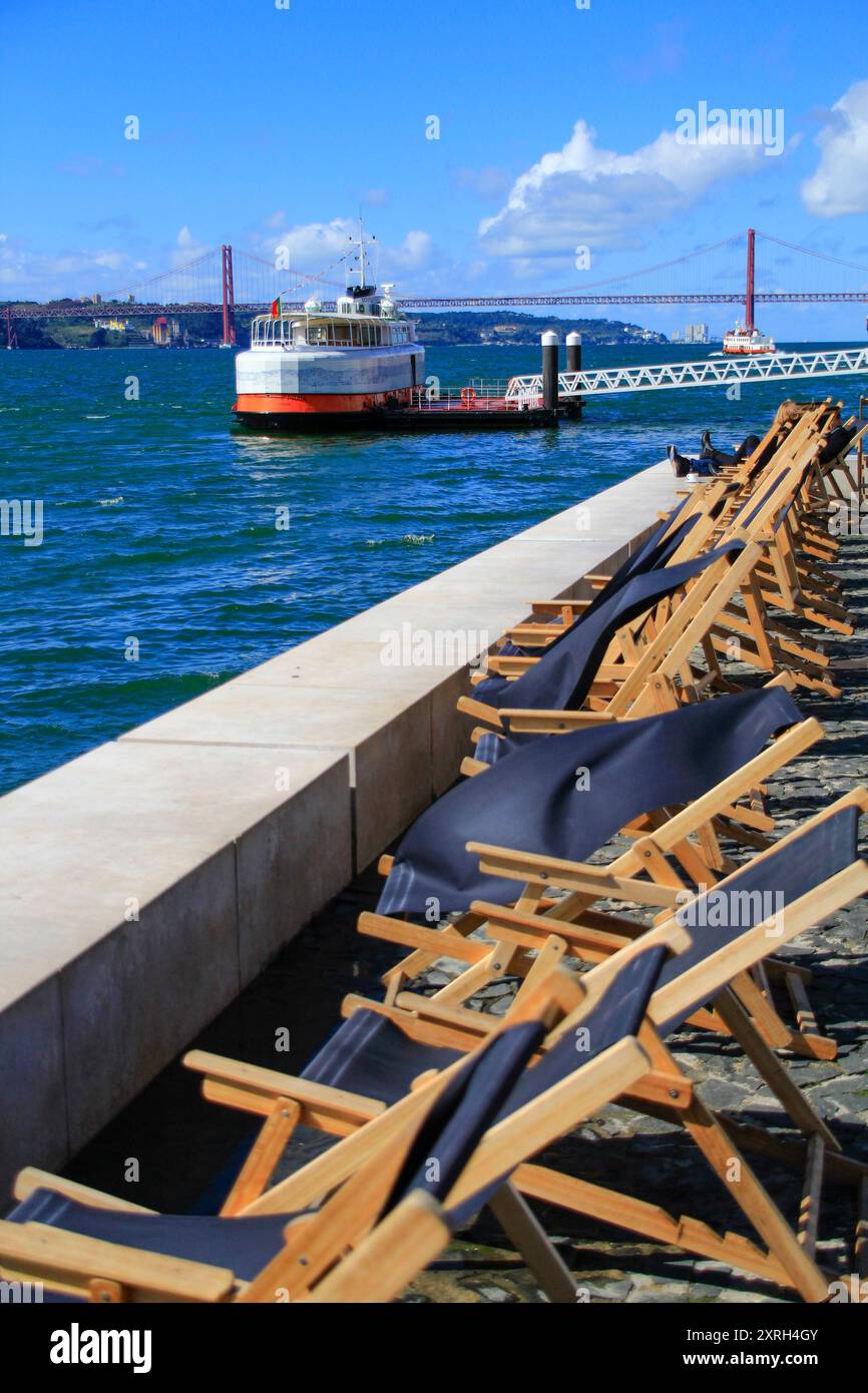 Lissabon, Portugal. Liegestühle am Fluss Tejo mit Blick auf die Brücke vom 25. April. März 2017 Stockfoto