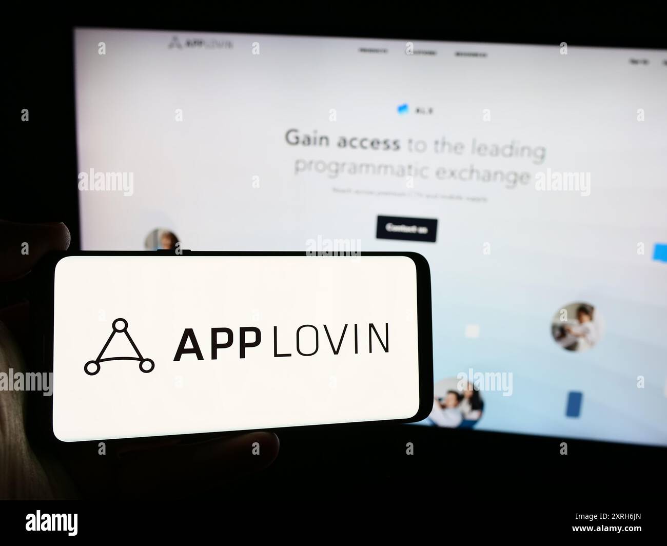 Person, die ein Mobiltelefon mit dem Logo des US-amerikanischen Mobiltechnologieunternehmens AppLovin Corporation vor der Unternehmenswebsite hält. Schwerpunkt auf dem Display des Telefons. Stockfoto