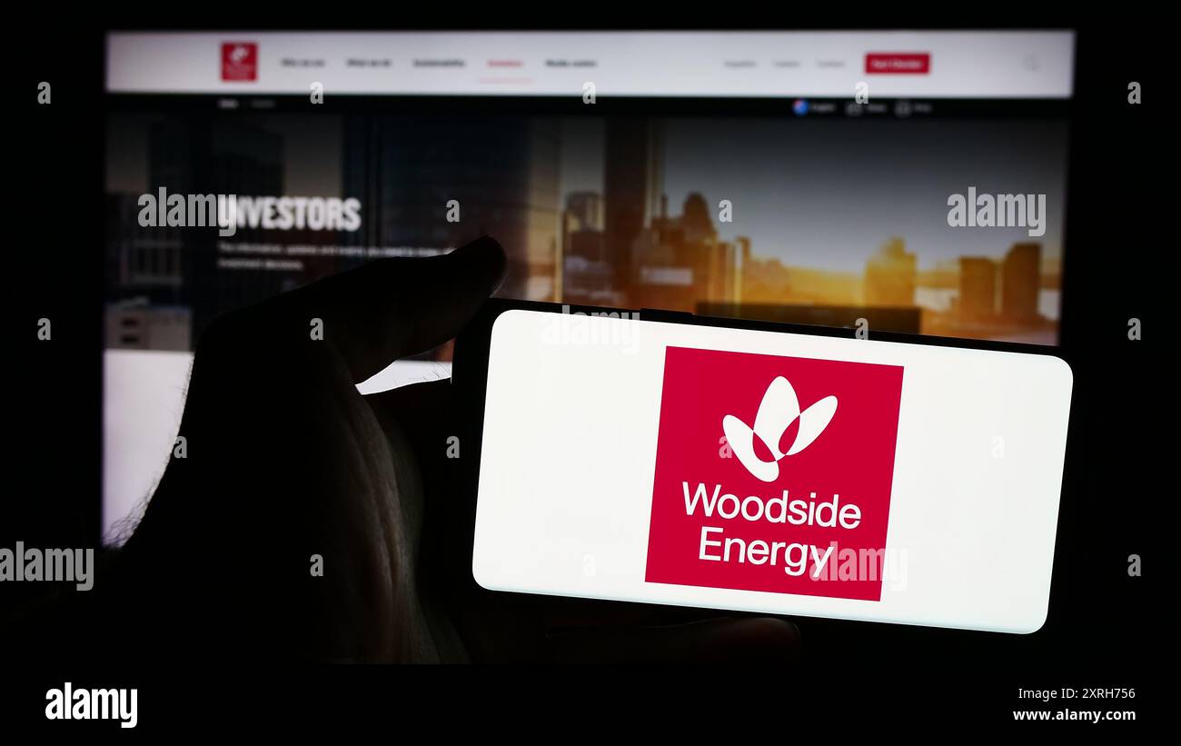 Person, die ein Mobiltelefon mit dem Logo des australischen Unternehmens Woodside Energy Group Limited vor der Webseite des Unternehmens hält. Schwerpunkt auf dem Display des Telefons. Stockfoto