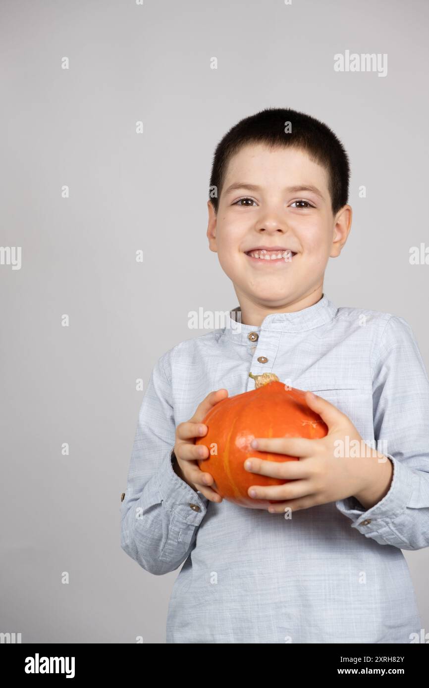 Glücklicher siebenjähriger Junge, der Hokkaido Kürbis hält und lächelt Stockfoto