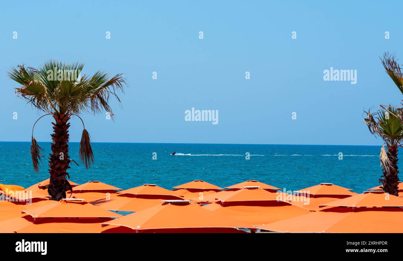 Die ruhige Oberfläche des Meeres über den Dächern von leuchtend orangefarbenen Sonnenschirmen Stockfoto