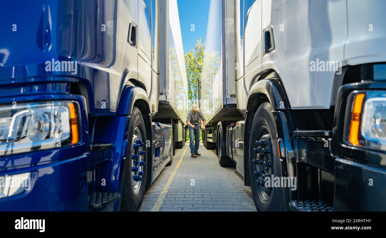 Eine Person überprüft die Lücke zwischen zwei geparkten Lkws auf einem Transportplatz unter klarem blauen Himmel. Stockfoto