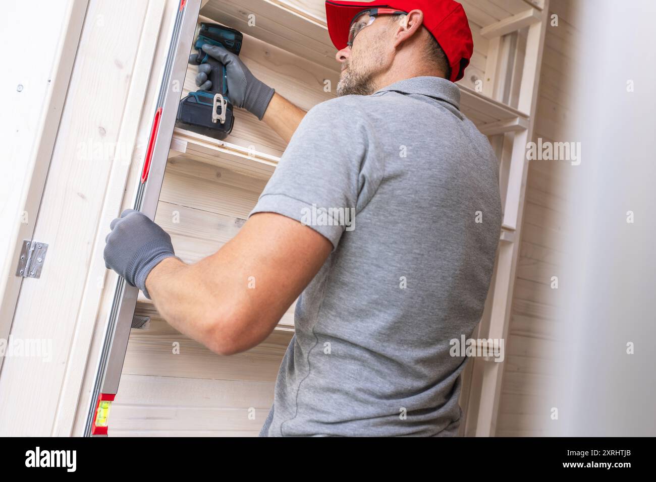 Ein geschulter Zimmermann konzentriert sich auf die Installation von Regalen in einer gut beleuchteten Heimwerkstatt mit einem Elektrowerkzeug für Präzision. Stockfoto