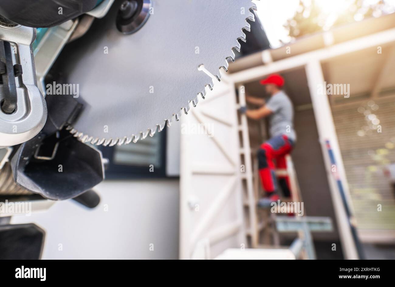 Ein Bauarbeiter bedient eine Kreissäge, während er auf einer Leiter sitzt und an einem Außenprojekt in einem Haus arbeitet. Stockfoto