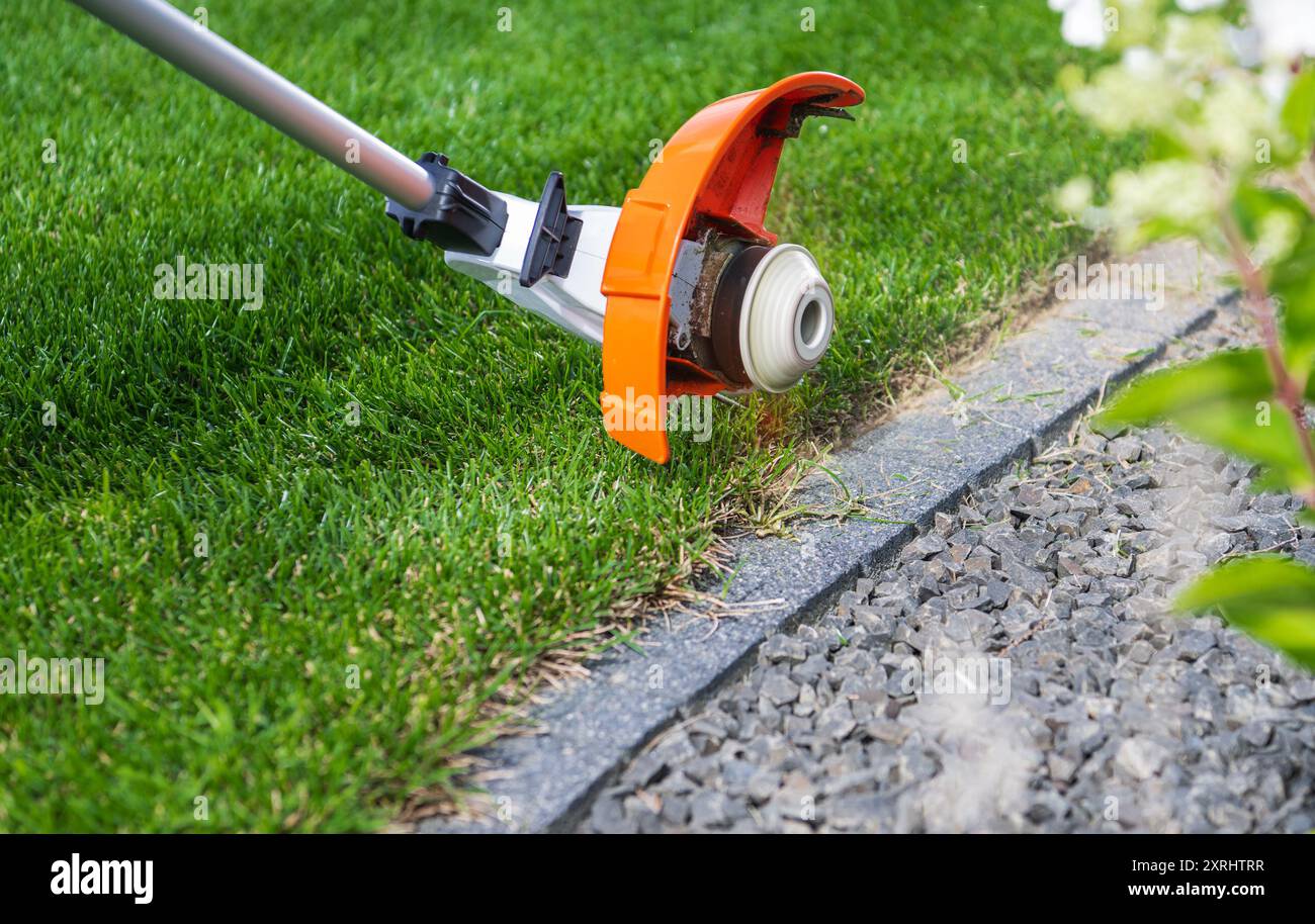 Eine Person schneidet das Gras mit einem Rasentrimmer nahe an einer Steinkante, um ein ordentliches Aussehen des Gartens zu gewährleisten. Stockfoto