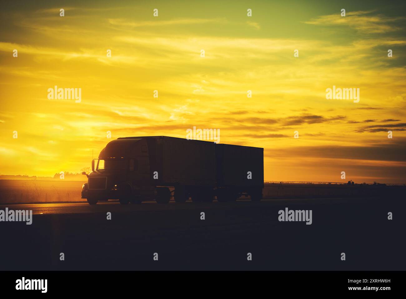 Bei Sonnenuntergang fährt ein Lkw eine offene Autobahn hinunter und wirft einen warmen goldenen Glanz über den Horizont und beleuchtet die Landschaft. Stockfoto