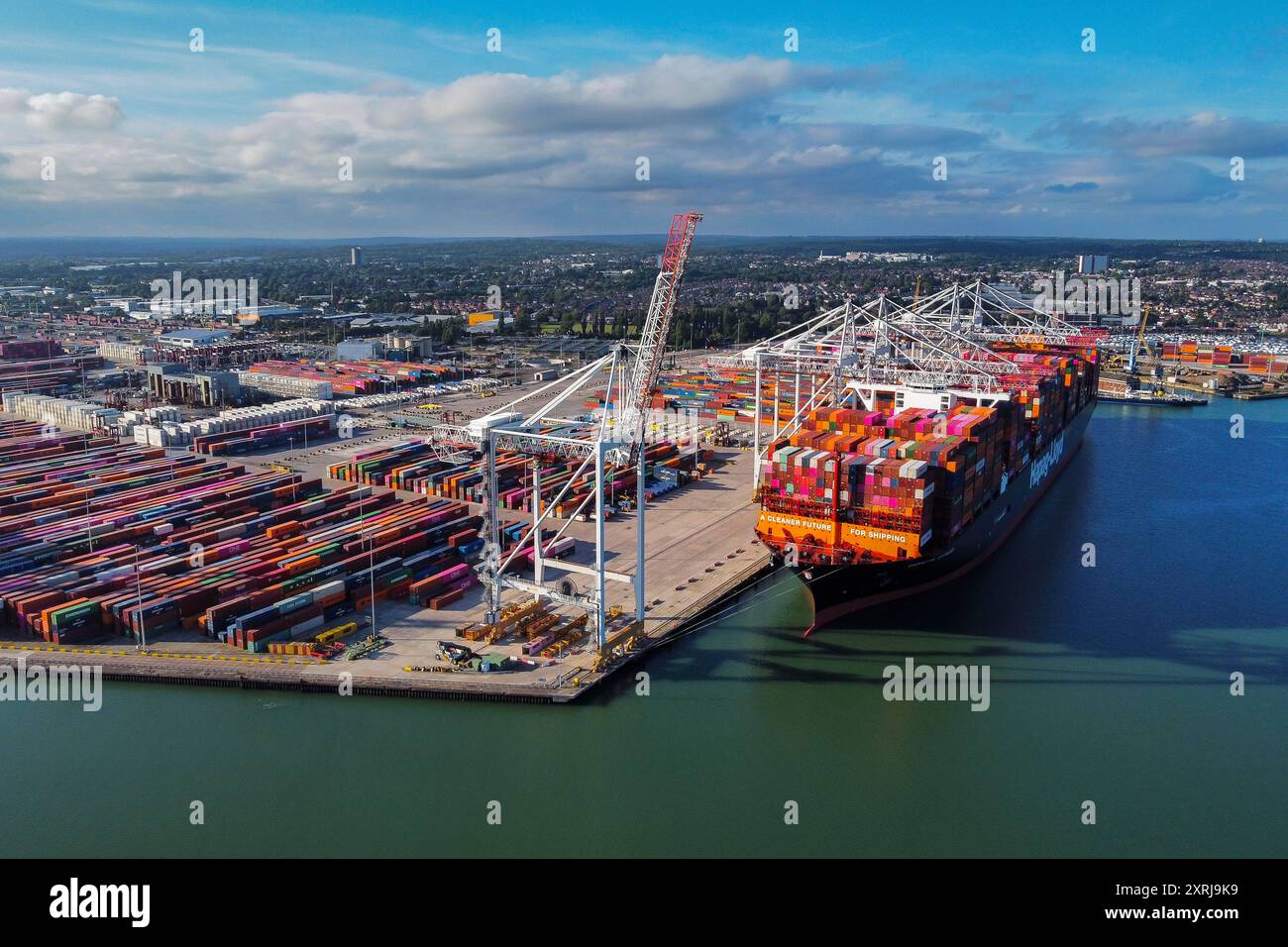 Southampton, Hampshire, Großbritannien. August 2024. Allgemeine Luftaufnahme der Western Docks im Hafen von Southampton in Hampshire mit dem Hapag-Lloyd-Containerschiff Damietta Express, das die Botschaft „A Cleaner Future for Shipping“ trägt. Nach dem Hafen von Felixstowe ist Southampton das zweitgrößte Containerterminal im Vereinigten Königreich, das den Verkehr von 1,5 Millionen TEU-Einheiten umfasste. Bildnachweis: Graham Hunt/Alamy Live News Stockfoto