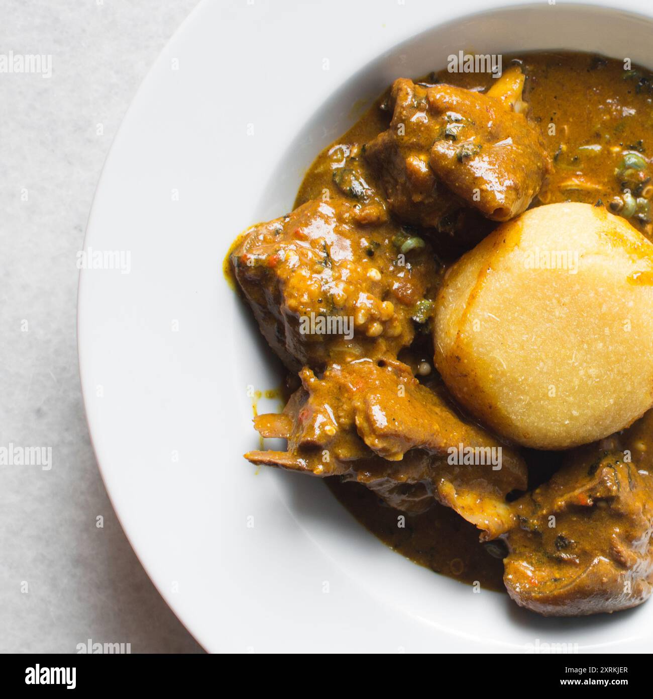 Blick von oben auf nigerianische Ogbono-Suppe und eba auf einem weißen Teller, Blick von oben auf Ogbono-Suppe mit garri und verschiedenen Fleischsorten auf einem Suppenteller Stockfoto