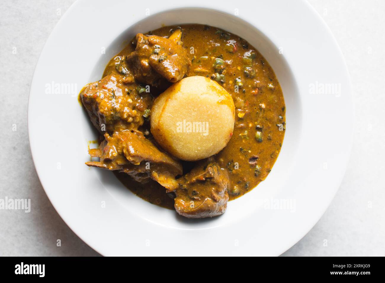 Blick von oben auf nigerianische Ogbono-Suppe und eba auf einem weißen Teller, Blick von oben auf Ogbono-Suppe mit garri und verschiedenen Fleischsorten auf einem Suppenteller Stockfoto