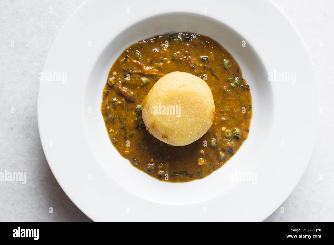 Blick von oben auf nigerianische Ogbono-Suppe und eba auf einem weißen ...