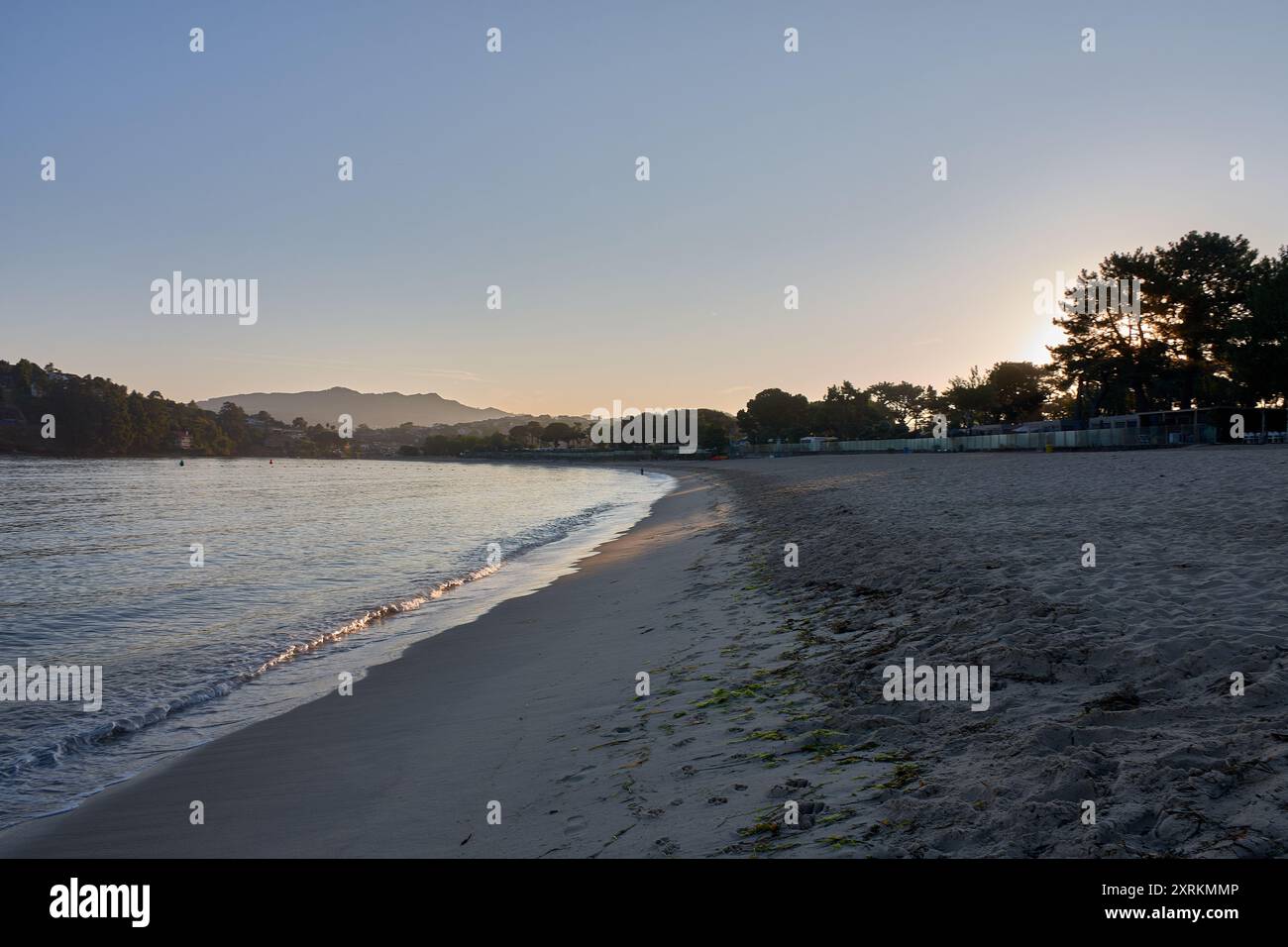 Die atemberaubende Schönheit der Playa de la Ladeira in Baiona bei Sonnenaufgang. Wenn die Sonne aufgeht, taucht ihr goldenes Licht den Sandstrand und das ruhige Wasser und schafft so Stockfoto