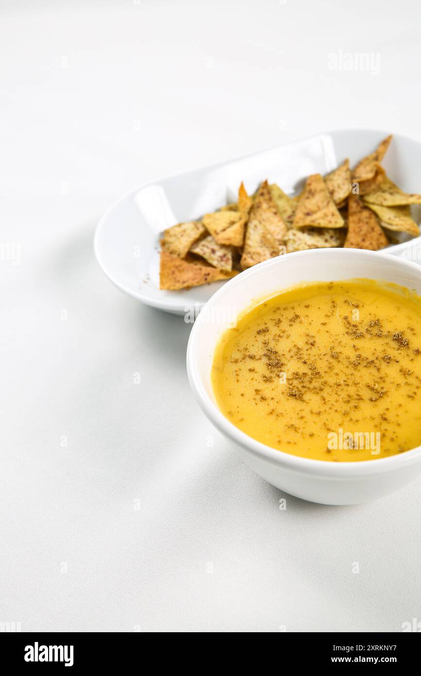Kürbiscremesuppe in weißer Schüssel mit dünnen Brotchips auf weißem Tisch Stockfoto