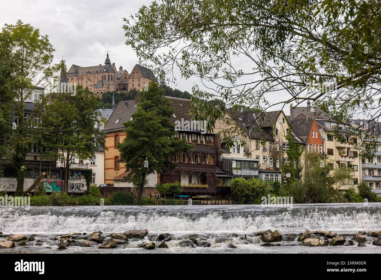 Marburg, Deutschland. August 2024. Die Marburger Burg, auch Landgrafenburg Marburg genannt, erhebt sich über der Stadt. Blick vom Ufer der Lahn über die Häuser des südlichen Viertels hinauf auf den Burgberg. Sie entstand im 11. Jahrhundert als Burg und wurde im 13. Jahrhundert von den Landgrafen von Hessen in ein Wohnschloss umgewandelt. Seit 1981 beherbergt das Schloss das Kunstgeschichtliche Museum der Philipps-Universität Marburg. Quelle: Christian Lademann/dpa/Alamy Live News Stockfoto
