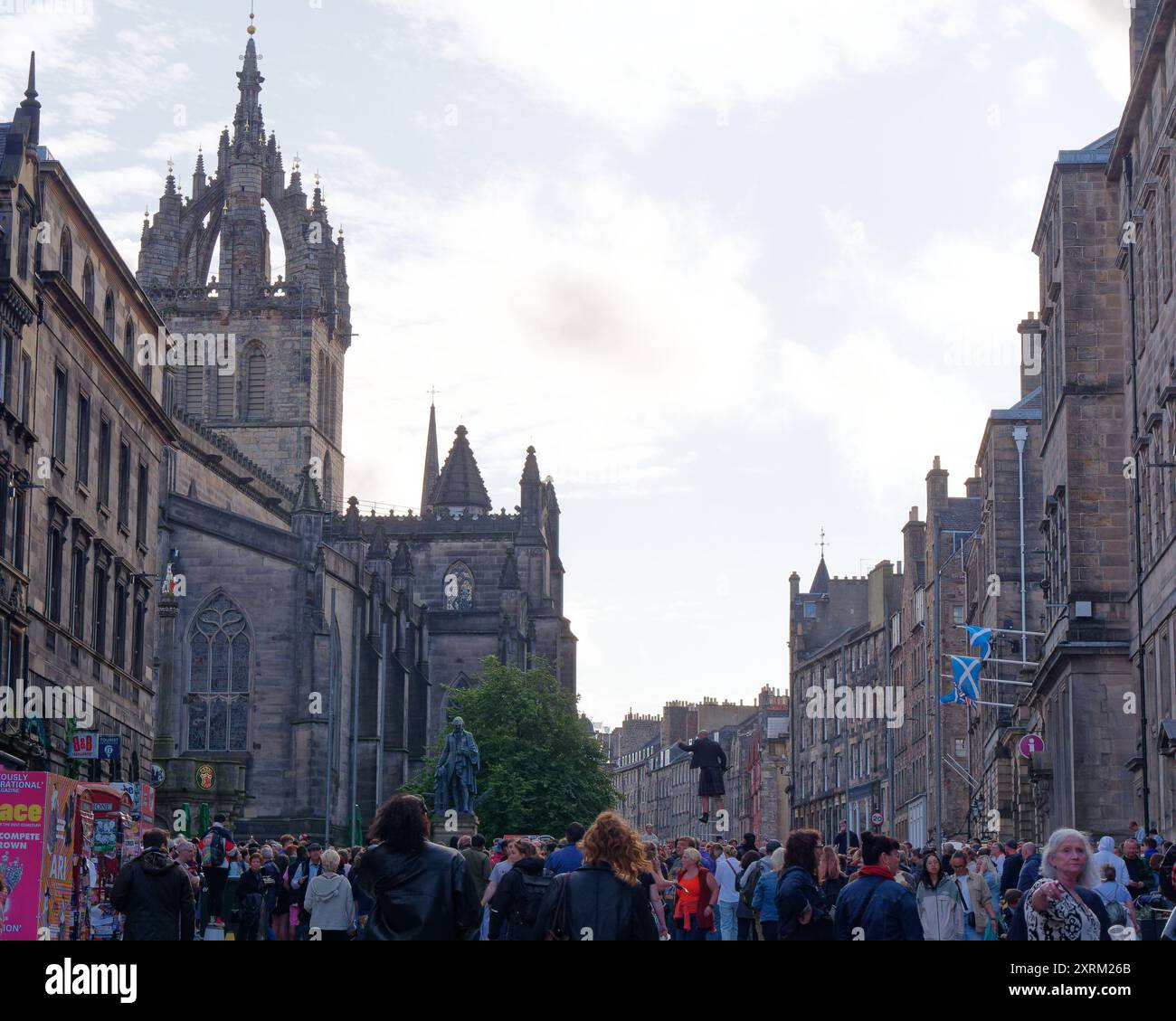 Mann auf Stelzen inmitten der Menschenmassen auf der Royal Mile mit der St. Giles Church hinter dem Fringe Festival in Edinburgh Schottland. August 2024 Stockfoto