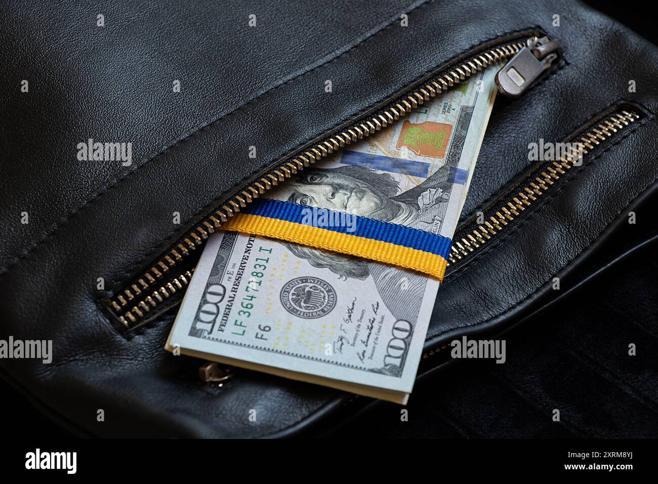 Band in Form der Flagge der Ukraine, gebunden auf einem Stapel von Hundert-Dollar-Scheinen in der Tasche eines schwarzen Mannes, finanzielle Hilfe für die Ukraine Stockfoto