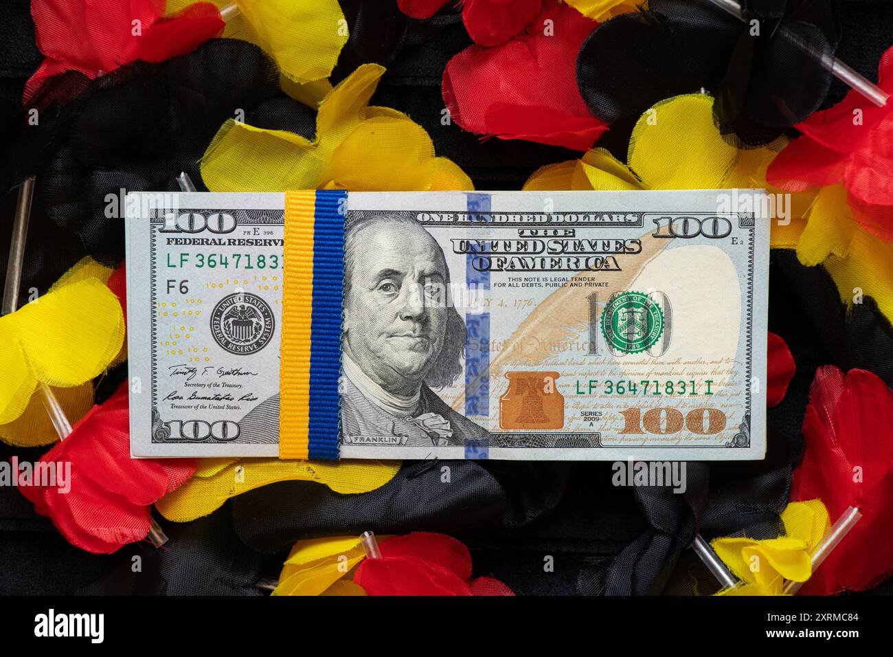Ein Band in Form der ukrainischen Flagge, gebunden auf einem Paket von Hundert-Dollar-Scheinen, liegt auf der deutschen Flagge, finanzielle Hilfe für die Ukraine aus Deutschland Stockfoto