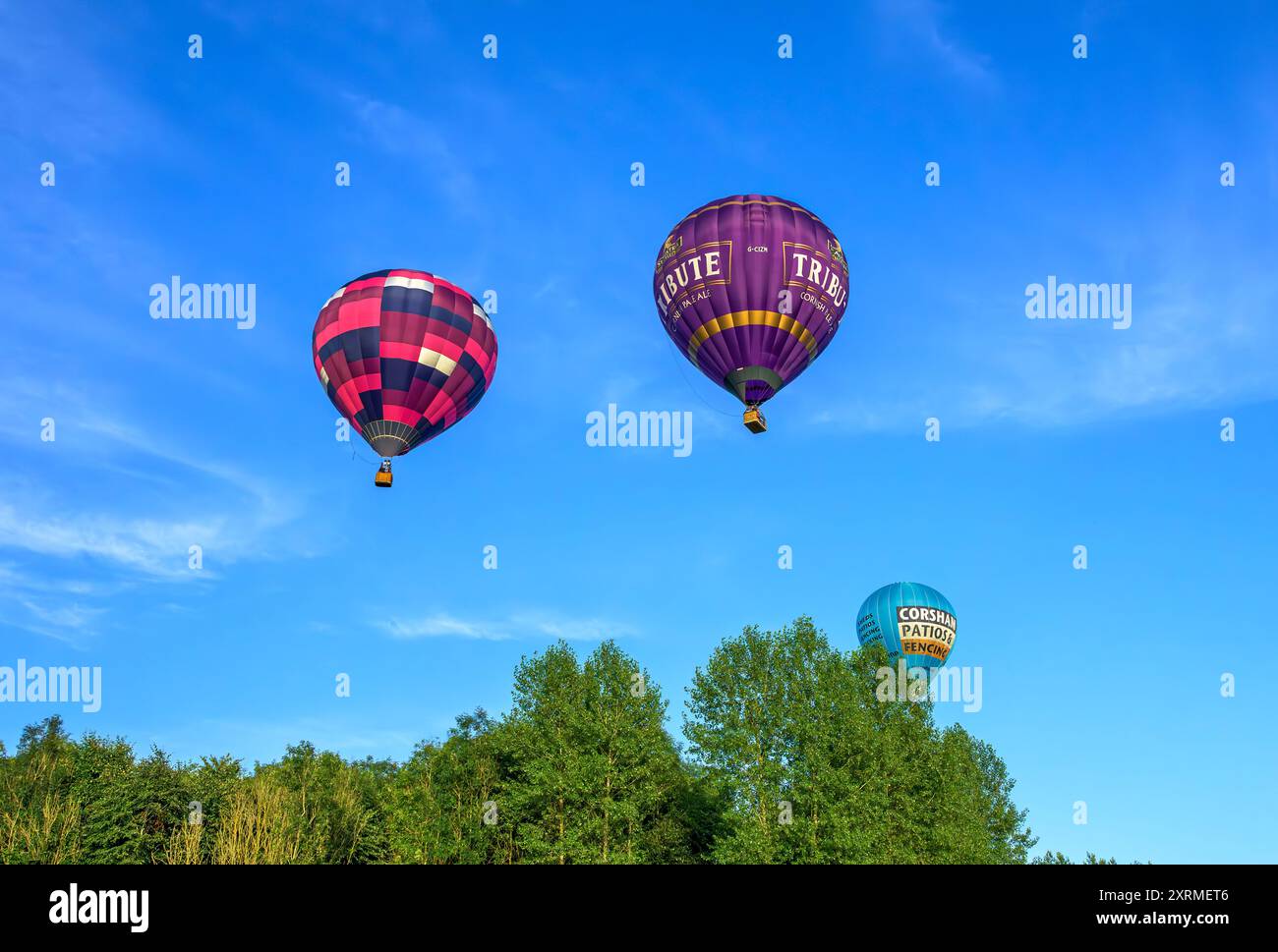 Farbenfrohe, sonnendurchflutete Ballons in der goldenen Stunde, von der Bristol Balloon Fiesta 2024, als sie über Bäume in der Nähe von Siston; Bristol passieren. Am Samstag um 45 Uhr Stockfoto