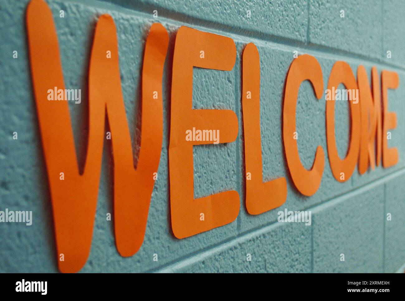 Ein Willkommensschild aus orangefarbenem Bastelpapier an einer Wand aus Schlackenblöcken in einem Klassenzimmer. Stockfoto