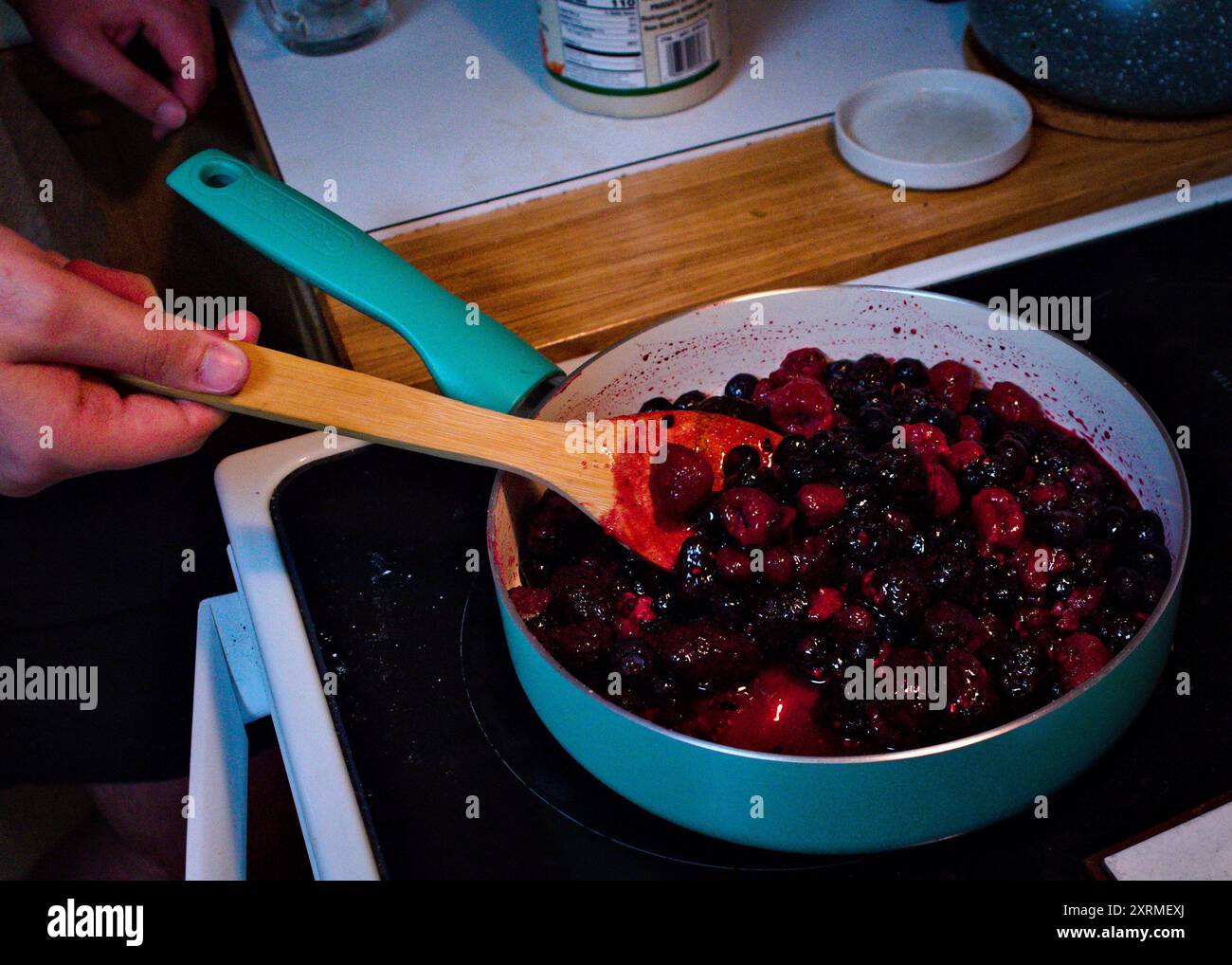 Ein junger Mann, der etwas Obst in einer Pfanne auf dem Herd kocht, während er einen Obstkuchen macht. Stockfoto