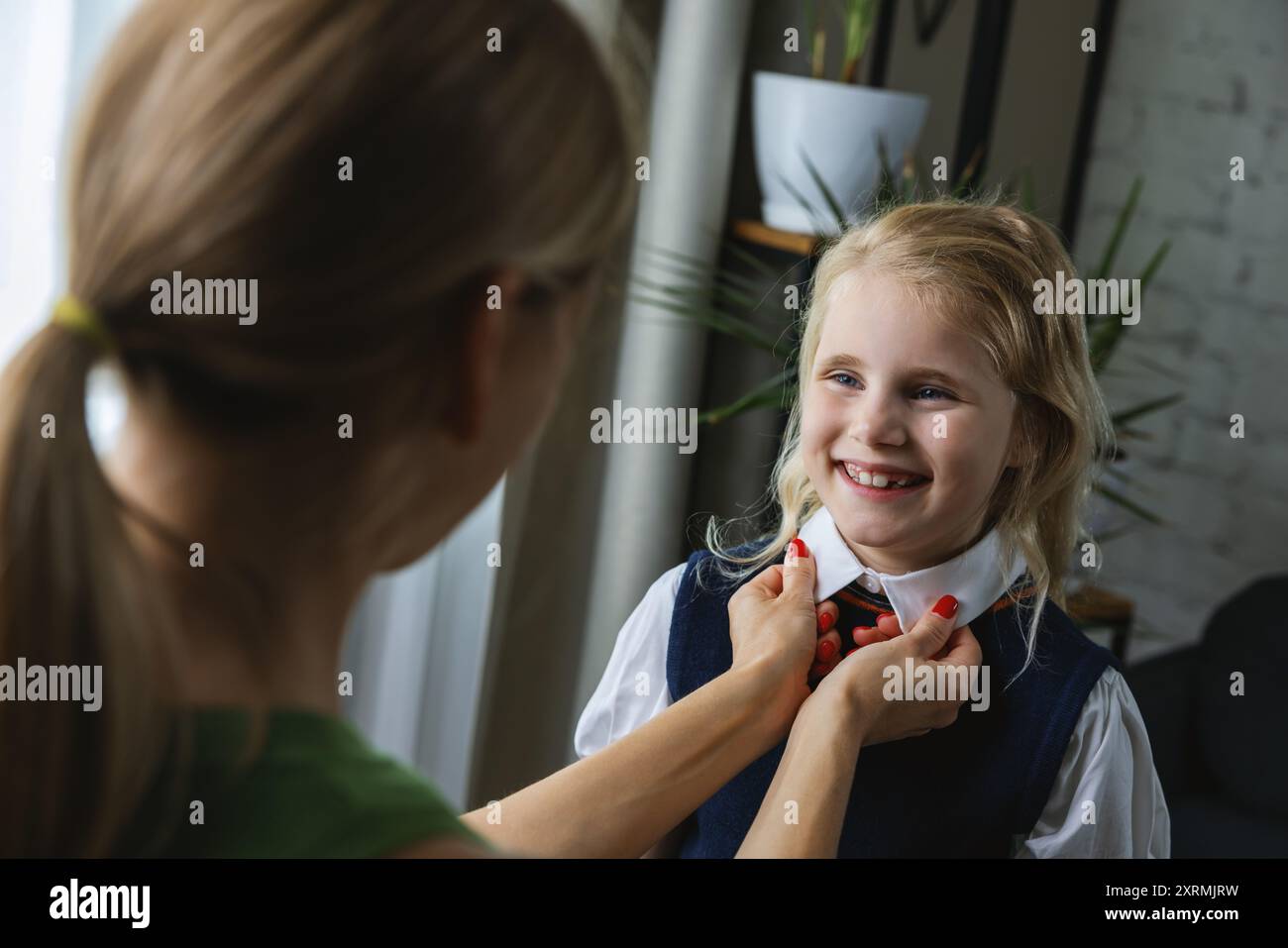 Mutter hilft und unterstützt ihre Tochter, sich auf den ersten Schultag im Wohnzimmer zuhause vorzubereiten Stockfoto