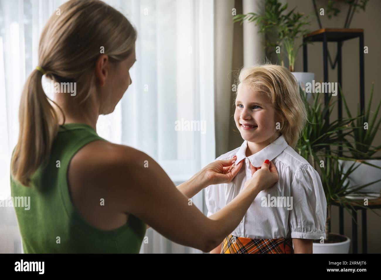 Mutter hilft, sich anzuziehen und unterstützt ihre Tochter, sich auf den ersten Schultag zu Hause vorzubereiten Stockfoto