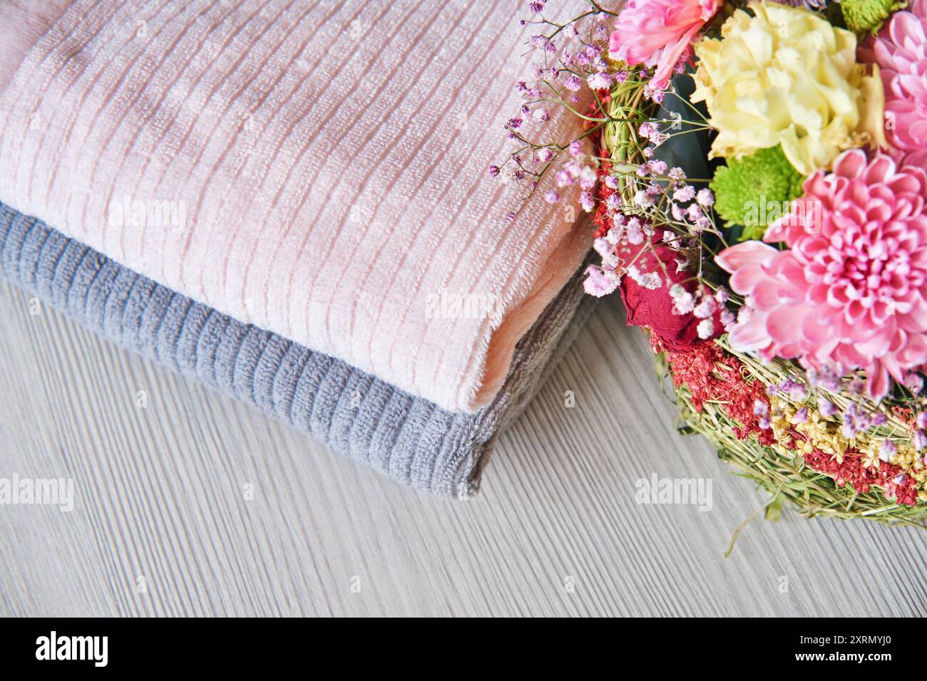 Ein Stapel Handtücher und wunderschöne Blumen. Hygiene-, Stoff-, Spa- und Textilkonzept. Baumwollhandtücher in Pastellfarben. Stockfoto