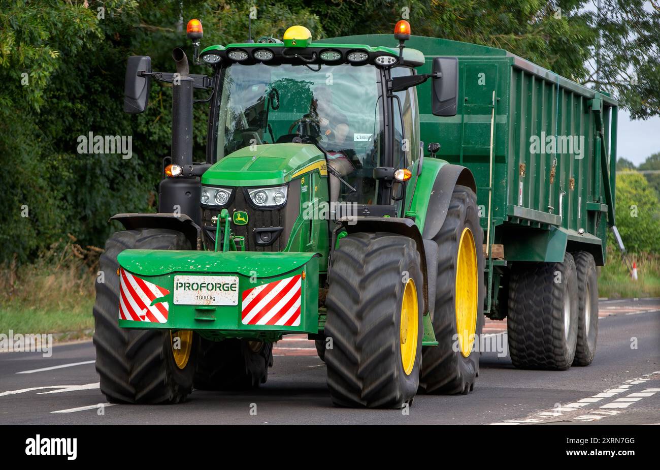 Potterspury, Northants, Großbritannien - 11. August 2024: Grüner John Deere 6r-Traktor zieht einen Anhänger auf einer britischen Landstraße Stockfoto
