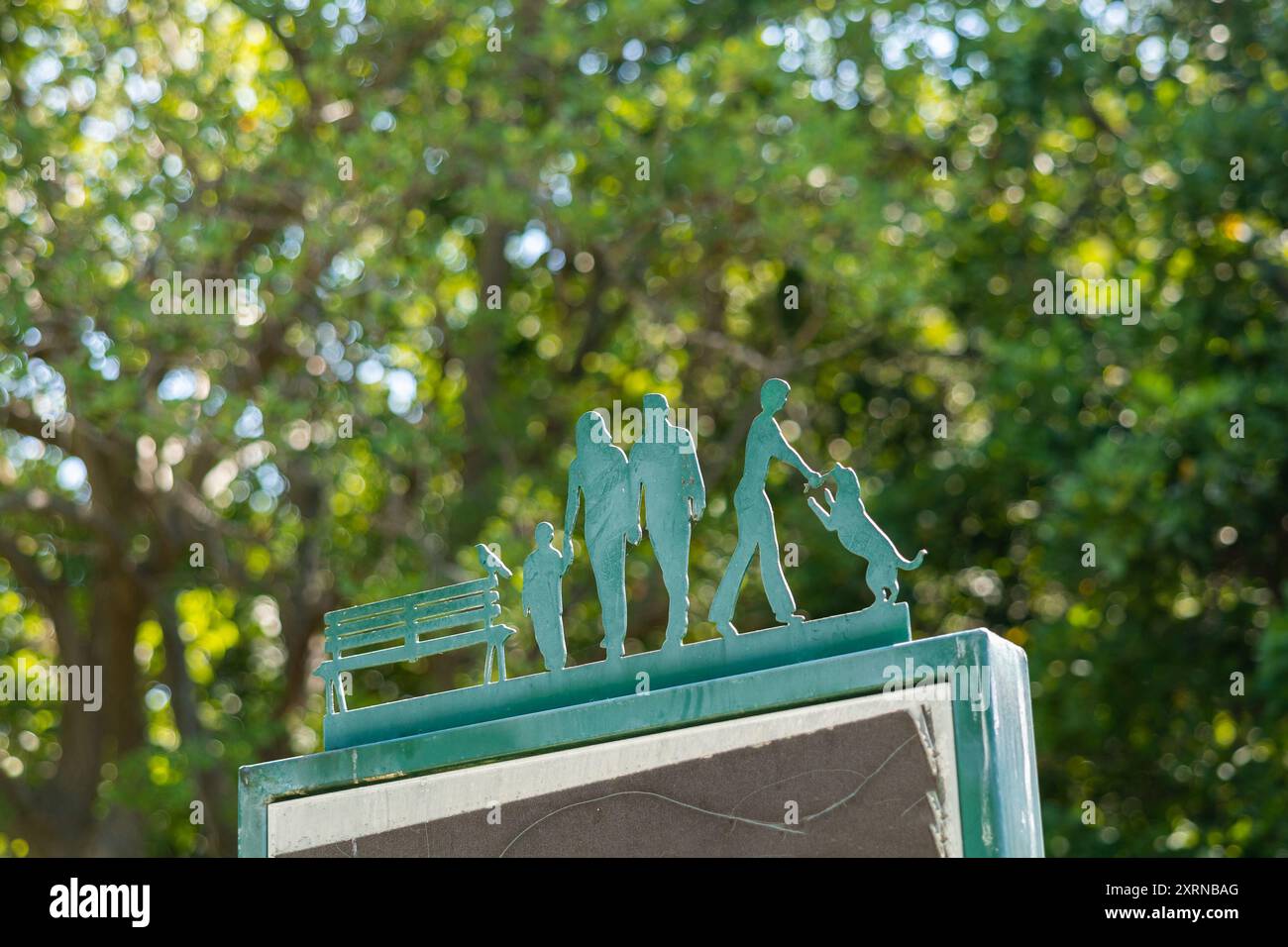 Dekorative Elemente aus Stahl mit Personensilhouetten in einem Park. Familie mit Kind, Hundebesitzer mit Haustier, Vogel auf einer Bank. Wunderschönes Bokeh im Hintergrund Stockfoto