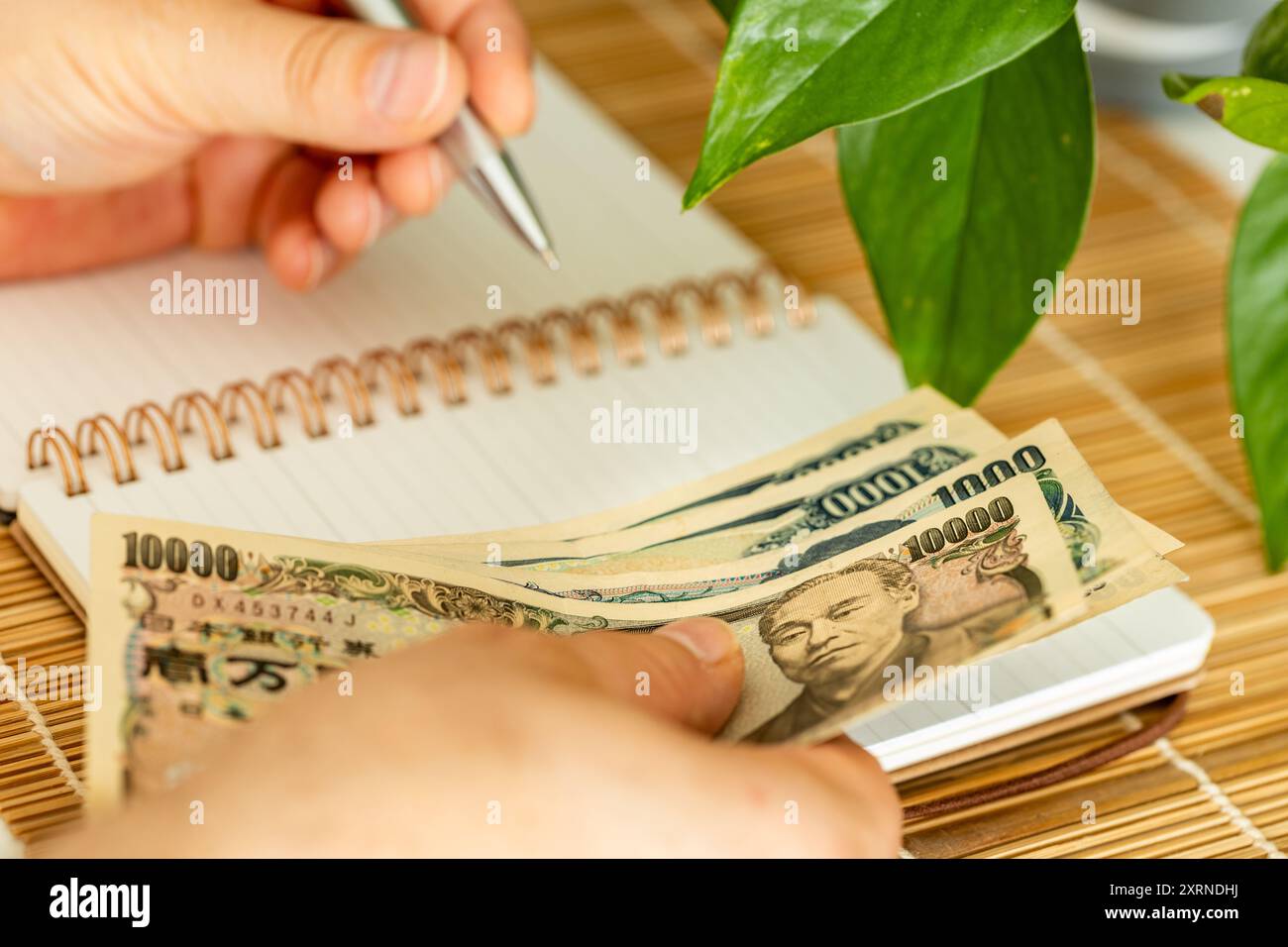 Ein Japaner, der Geld in der Hand hält und seine Einnahmen und Ausgaben in ein Notizbuch schreibt. Eine japanische Art, einen Haushalt zu retten und zu kontrollieren Stockfoto