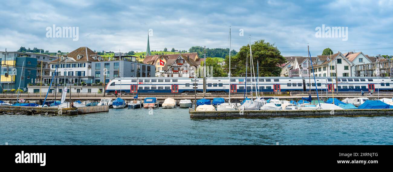 Wadenschwil, Schweiz - 1. Juli 2024: Ein Zug der Schweizerischen Bahn fährt am Zürcher See am Jachthafen in Wadenswil vorbei Stockfoto