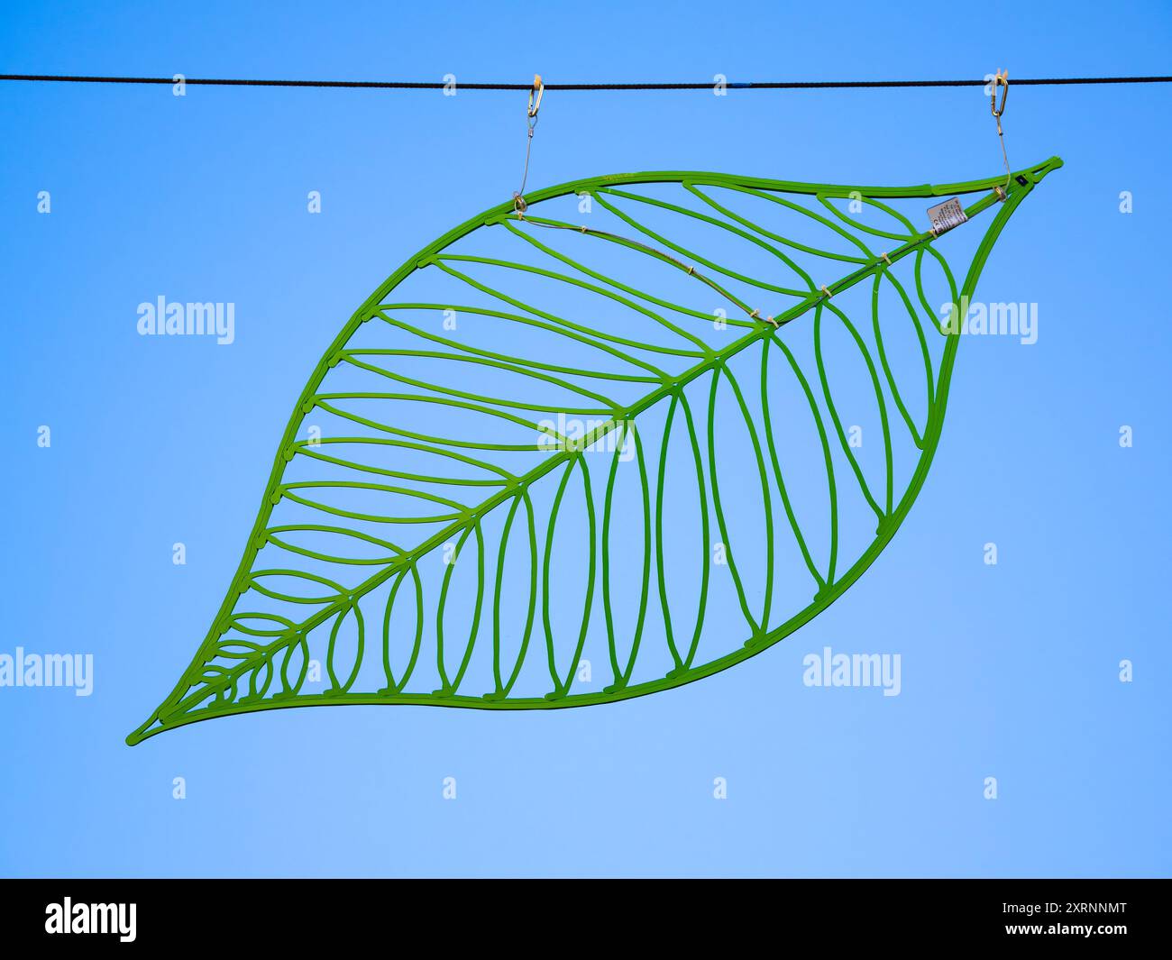 Montlucon, Frankreich - 18. Juli 2024: Stilvolles, dekoratives grünes Blatt, das an einem Draht vor blauem Himmel hängt. Stockfoto