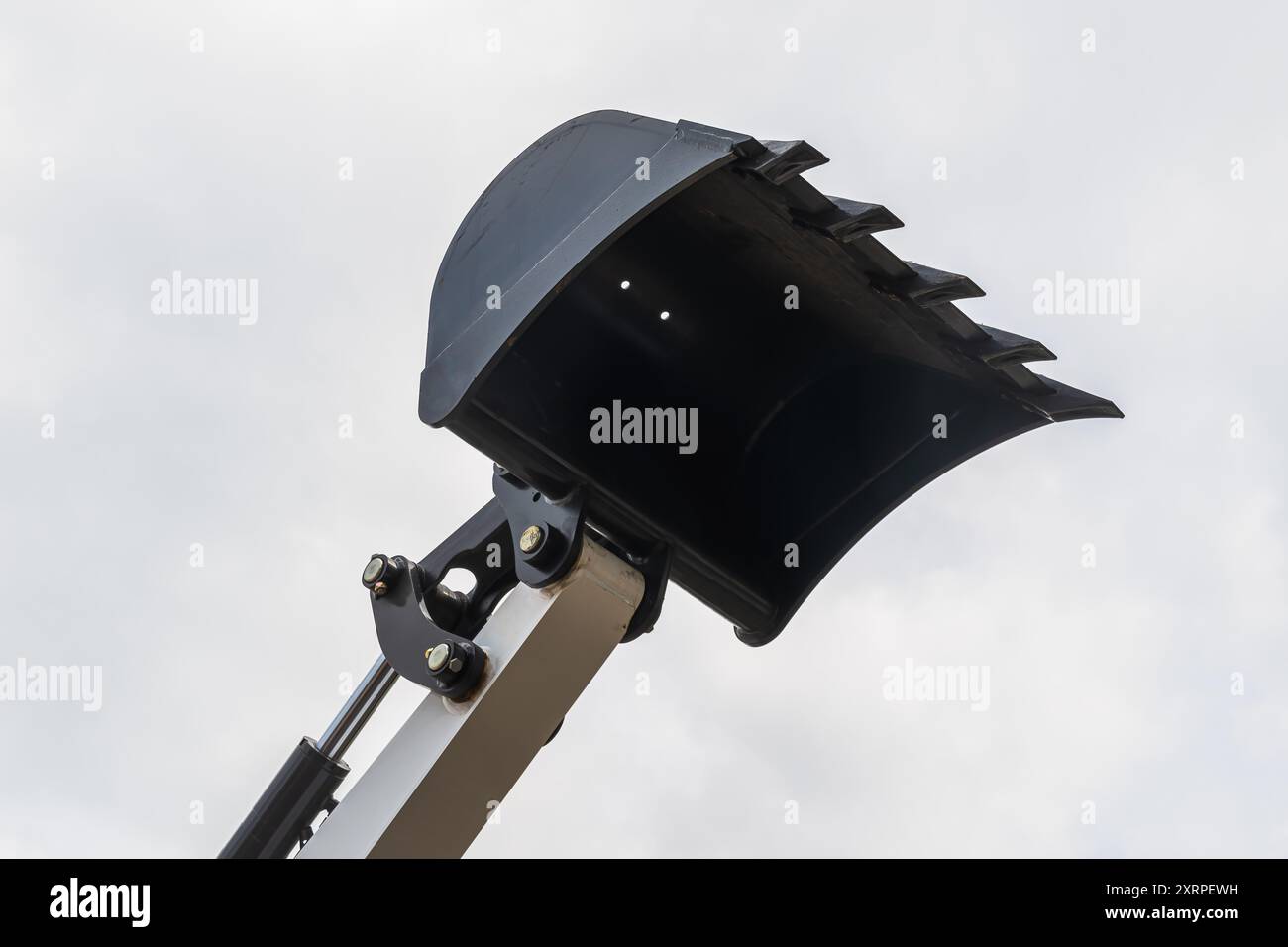 Baggerlöffel aus schwarzem Metall, Teil schwerer Baumaschinen, gegen einen bewölkten Himmel angehoben, zeigt seine Stärke und Nutzbarkeit im Bau p Stockfoto