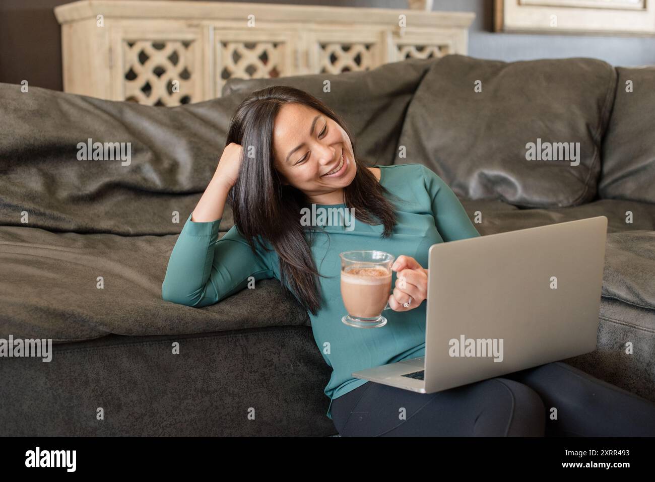 Glückliche asiatische Frau, die einen Laptop mit einem Becher ansieht Stockfoto