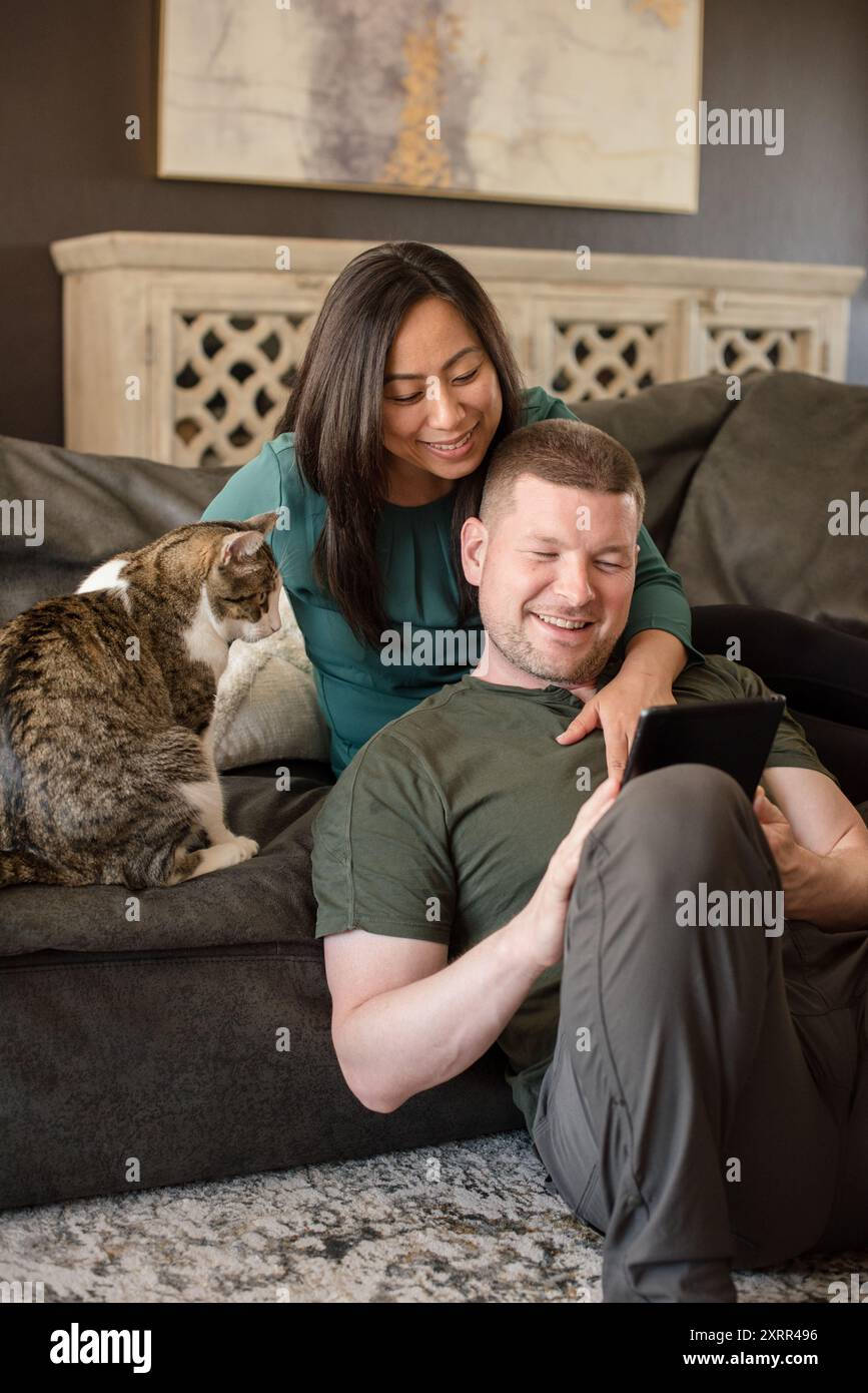 Ein Paar, das sich entspannt und sich eine Tablette mit einer Katze ansieht Stockfoto