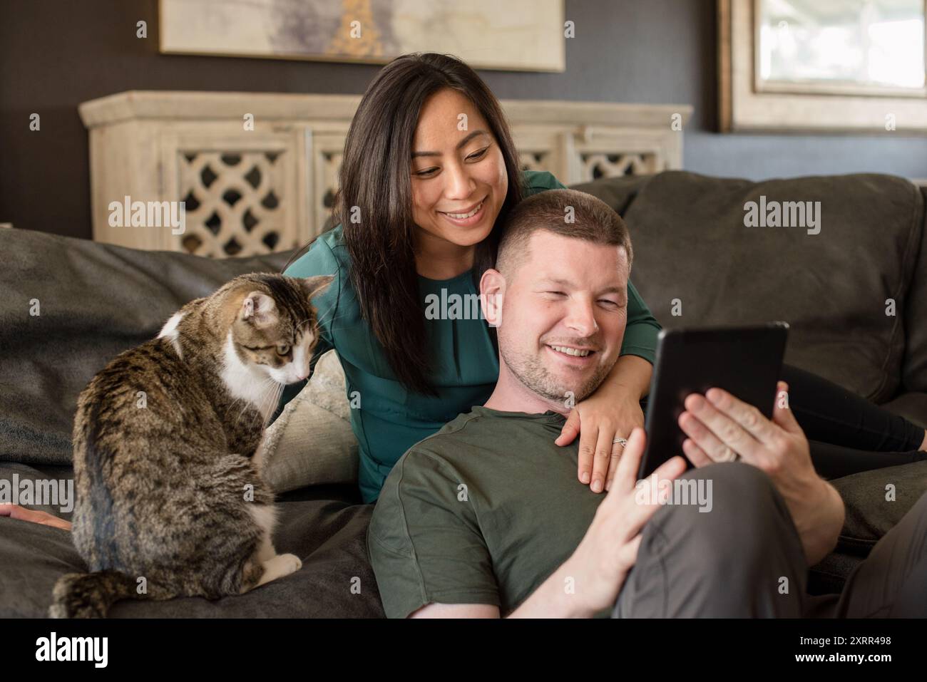 Ein Paar und eine Katze, die zusammen auf eine Tablette schauen Stockfoto