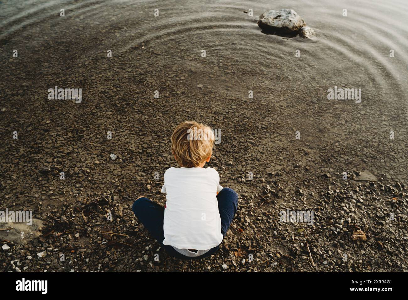 Rückansicht eines weißen Kindes, das mit Steinen am See spielt Stockfoto